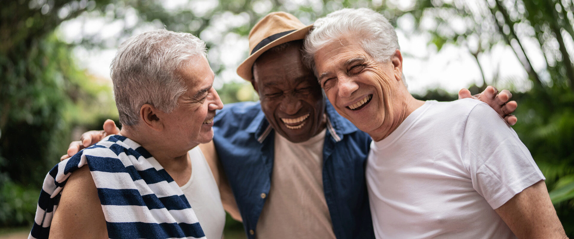 Three older adults laughing and embracing outdoors, representing friendship and joy.