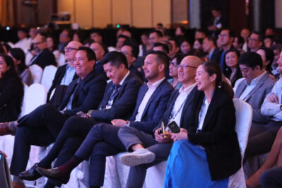 An audience in formal attire sitting and smiling at a conference or seminar.