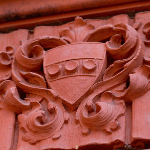 An ornate stone carving featuring a shield with three circles in a row, surrounded by decorative scrollwork.