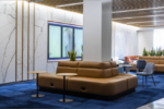 A modern university lobby with a sleek design features leather seating, blue carpeting, and marble walls. The Wharton School logo is displayed on one wall.