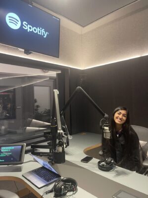 Shreya Krishnan, W’26 sits in a recording studio with a microphone, laptop, and Spotify logo on the screen above her.