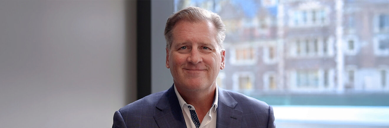 Rick Bates, WG'96 in blue suit with a blurred building in the background