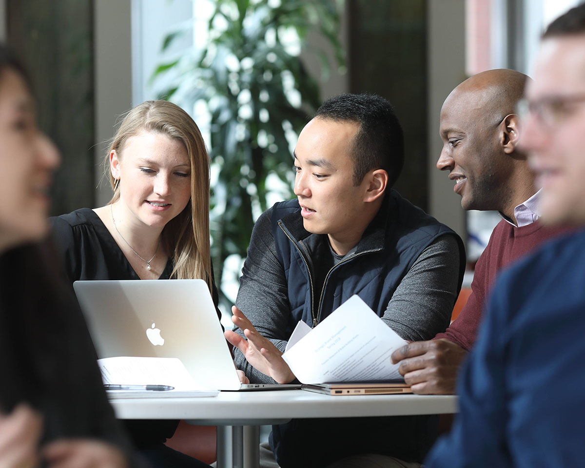 Wharton Online Course Image 4 Three Wharton alumni engaged in discussion around a laptop at a table indoors.