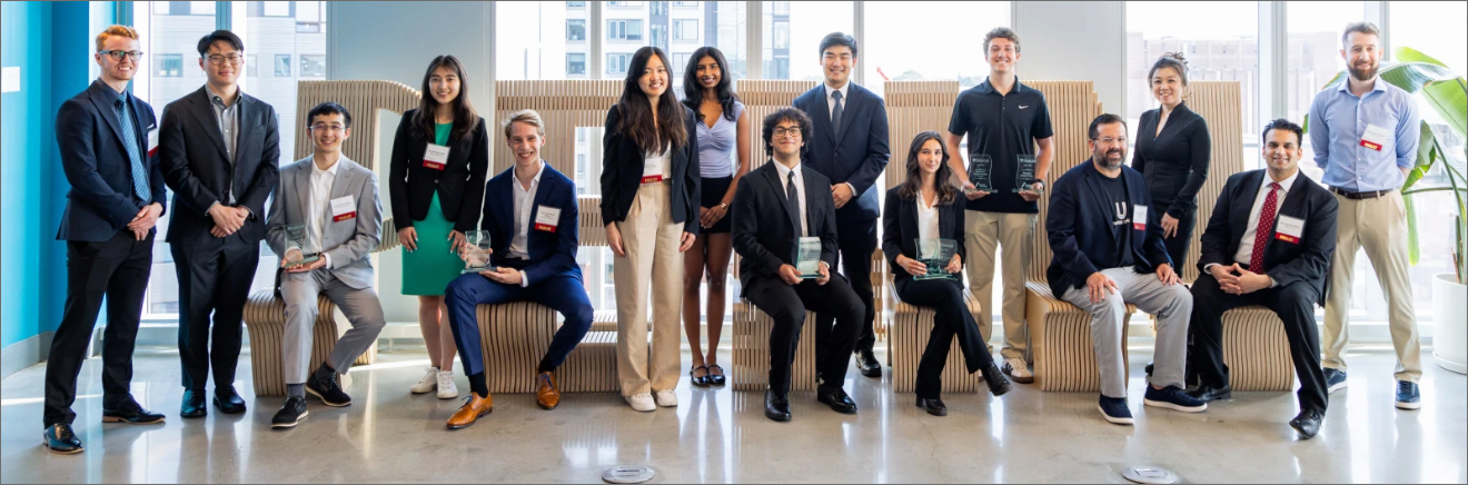 FY25-Impact-Newsletter-June-Story 3 A group of sixteen people representing the finalist teams at the 2025 Venture Lab Startup Challenge wear formal and smart casual attire and pose in Tangen Hall, some with plaques.