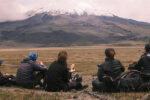 A group of Wharton students sitting in a field in Ecuador, observing a snow-capped mountain in the distance.