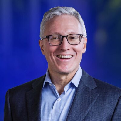 Professor John Paul MacDuffie in formal attire against a blue background.