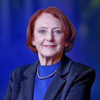 Professor Olivia Mitchell in formal attire against a blue background.