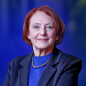 Professor Olivia Mitchell in formal attire against a blue background.
