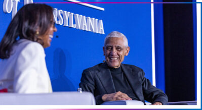A couple of people are seated and engaged in conversation on a stage. One person is smiling, and the backdrop displays the word "PENNSYLVANIA."