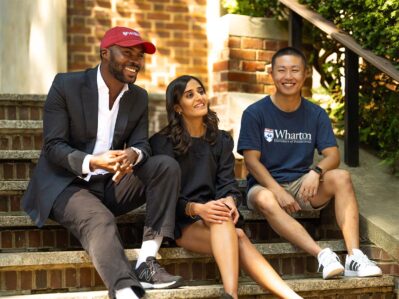 Three Wharton Fund Fellows sitting on brick steps outdoors, two men and a woman, relaxed and smiling.