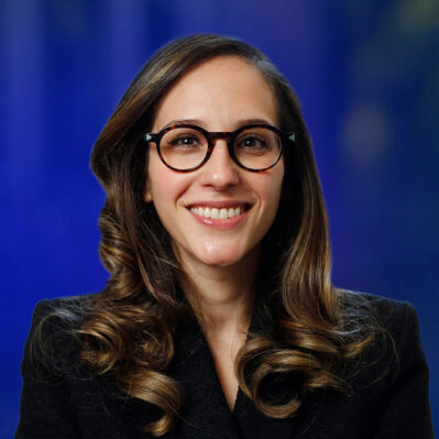 Shiri Melumad wearing glasses in front of a blue background