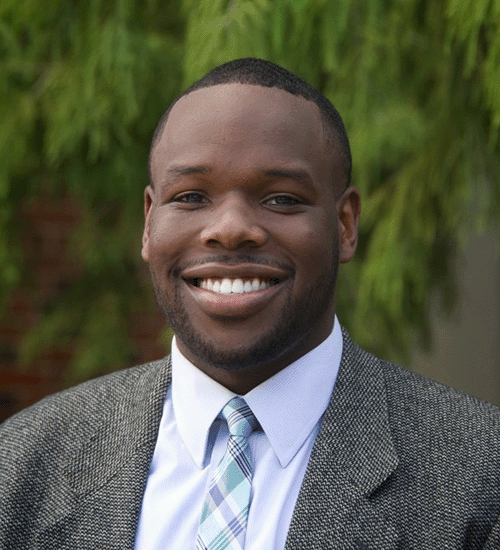 Andrew Udofa wearing a blazer, tie and smiling