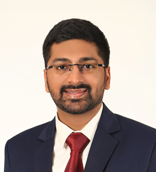 Satvik wearing glasses smiling, with a tie and blazer