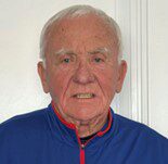 Headshot of a person with short white hair, wearing a blue jacket with a red zipper, against a plain background.
